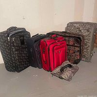 Photo showing five pieces of luggage: black XO patterned bag, navy bag, red bag, floral patterned bag, and small camouflage bag placed on the floor.