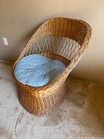 Bamboo wicker chair with curved back and arms, featuring blue floral cushion on seat, placed on carpet
