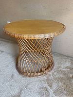 Full view of round bamboo side table showing woven cylindrical base and wooden top on carpeted floor.