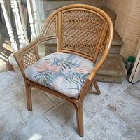 Front view of the cane chair sitting on a tile floor with floral cushion in place.