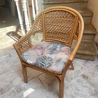 Full view of cane chair with floral cushion, showing front and side profile.