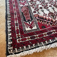 Close-up of corner showing fringe and part of patterned border with red, black and white colors