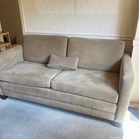 Front view of beige fabric three-seat couch with cushions, including lumbar pillow on one seat cushion.