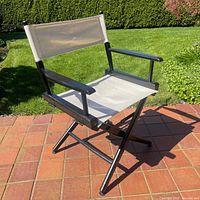 Front angle view of the directors chair showing the beige fabric seat and backrest with black wooden frame and armrests.