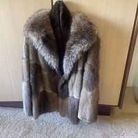 Full view of mid-length brown fur coat hanging against wooden panel