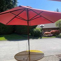 Wide shot of the round yellow metal patio table with red umbrella opened above it outdoors.