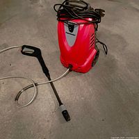 Red Husky Powerwasher with attached spray gun and hose on concrete floor.