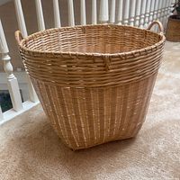 Large bamboo basket shown standing on carpet, clean condition, side handles visible.