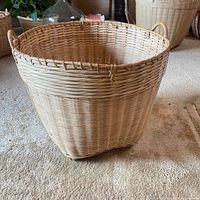 Side view of large round bamboo basket on carpet showing woven body and handles.