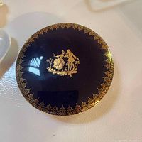 Top view of dark blue Limoges lidded dish lid with gold detailing of man and woman figures and ornate border.