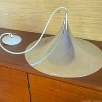 Full view of conical metal pendant shade and attached cord and canopy