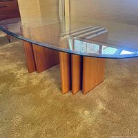 Front view of coffee table showing curved glass top resting on two slatted teak wood pedestal bases