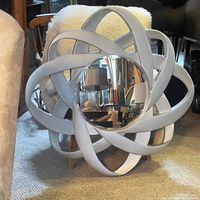 Full front view of the circular decorative wall mirror with silver interlocking petal-like frame and central reflective mirror.