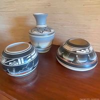 Photo showing set of three ceramic pottery pieces by Naatsiilid, various shapes and painted desert landscape and geometric patterns