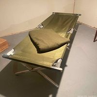 Full view of the collapsible army cot with olive green fabric and folded wool blanket on top.