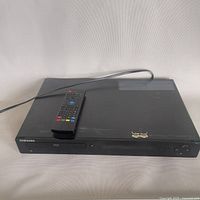 Full view of Samsung Blu-ray/DVD player showing disc tray, power button, and remote control on top.