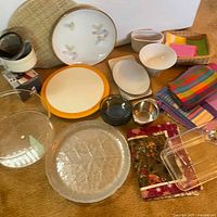 Wide view of lot showing plates, bowls, glass dishes, napkins, coasters, and dome cover