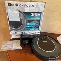 Box packaging showing Shark ION Robot R75 vacuum, charging dock, power adapter, and manual on table