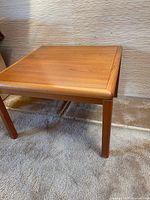 View of wooden side table showing corner, legs, and surface with visible wood grain.