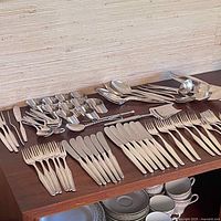 Full overview photo of the flatware and serving items laid out on the surface, showing arrangement of forks, knives, and spoons.