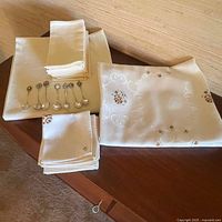 Photo showing folded table linens and six collector spoons arranged on top.