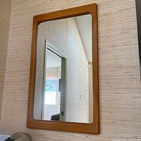 Full view of the rectangular teak framed mirror hanging on a textured wall.
