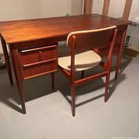 Full view of teak desk and matching chair on concrete floor