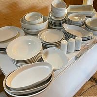 Wide view displaying the full assortment of white serving dishes, plates, bowls, and salt and pepper shakers on a table.