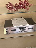Another front view of Yamaha KX-W282 stereo double cassette deck with user manual, showing clean silver finish, button controls, and headphone jack on the left.