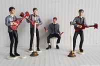 Group photo of all six Beatles figurines in gray shirts and black pants, holding instruments and drumsticks on white base.