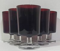 Front view of six ruby red goblets with clear bases, showing height and color