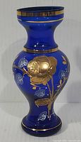 Front view of cobalt blue vintage Bohemian glass vase with gilt rose and floral decoration showing the overall shape and color.