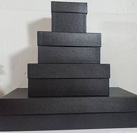 Four black nesting gift boxes stacked outside each other showing textured black exteriors and lids.