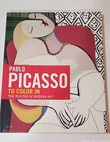 Front cover of the softcover colouring book. Shows a half colored, half line art Picasso painting of a reclining figure. Text: Pablo Picasso to color in the master of modern art.