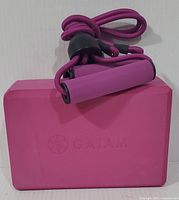 Pink GAIAM yoga block and pink resistance band with foam handles coiled on top of the block, both unused.