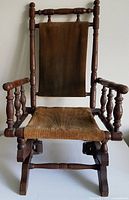 Front view of the children's rocking chair showing wooden frame, turned spindle arms, and fabric seat and backrest.