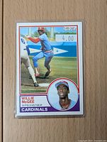 Front of the 1983 O-Pee-Chee Willie McGee rookie baseball card showing player in batting stance and inset headshot with team name Cardinals.