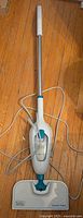 Front view of Black and Decker steam mop showing handle, control button, and power cord on wooden floor.