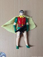 Front view of Robin action figure showing red and green costume, yellow cape, and black gun accessory attached to the figure.