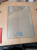 Three clear glass shelves laid flat on a wooden surface, two featuring silver-tone metal hinges, all in very good condition without scratches.