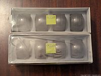 Two unopened boxes of Gluckstein Studio resin napkin rings, each containing 4 napkin rings with a smooth rounded design in light gray, visible through the packaging.