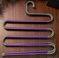 Four metal pants hangers with purple foam sleeves laid out flat on wooden surface arranged side by side to show design and condition.