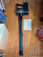 Photo of a PrettyCare cordless stick vacuum cleaner laid on wooden floor with instruction manual next to it.