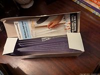 Opened box showing five purple metal $ record wall display brackets with hooks in original packaging