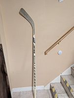 Full view of the Bauer hockey stick leaning against a wall showing the taped blade and shaft.