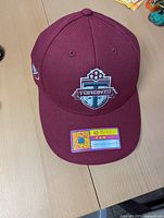Front view of maroon Toronto FC cap with embroidered club logo, holographic fan product sticker on brim.
