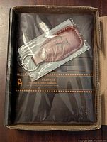 Photo of the vintage leather journal and leather key holder inside original packaging, showing the journal with dark brown leather and a leather pen holder, key holder sealed in plastic.