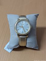 Front view of new womens Timex watch on grey cushion, showing gold-tone leather strap and gold-colored markers on white dial.