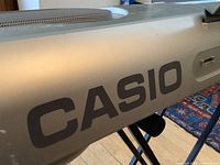 Close-up of Casio logo on the silver keyboard body showing part of built-in speaker grill and control area.