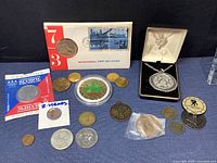 Coins, tokens, pendants, first day cover, and various commemorative pieces arranged on cloth surface.